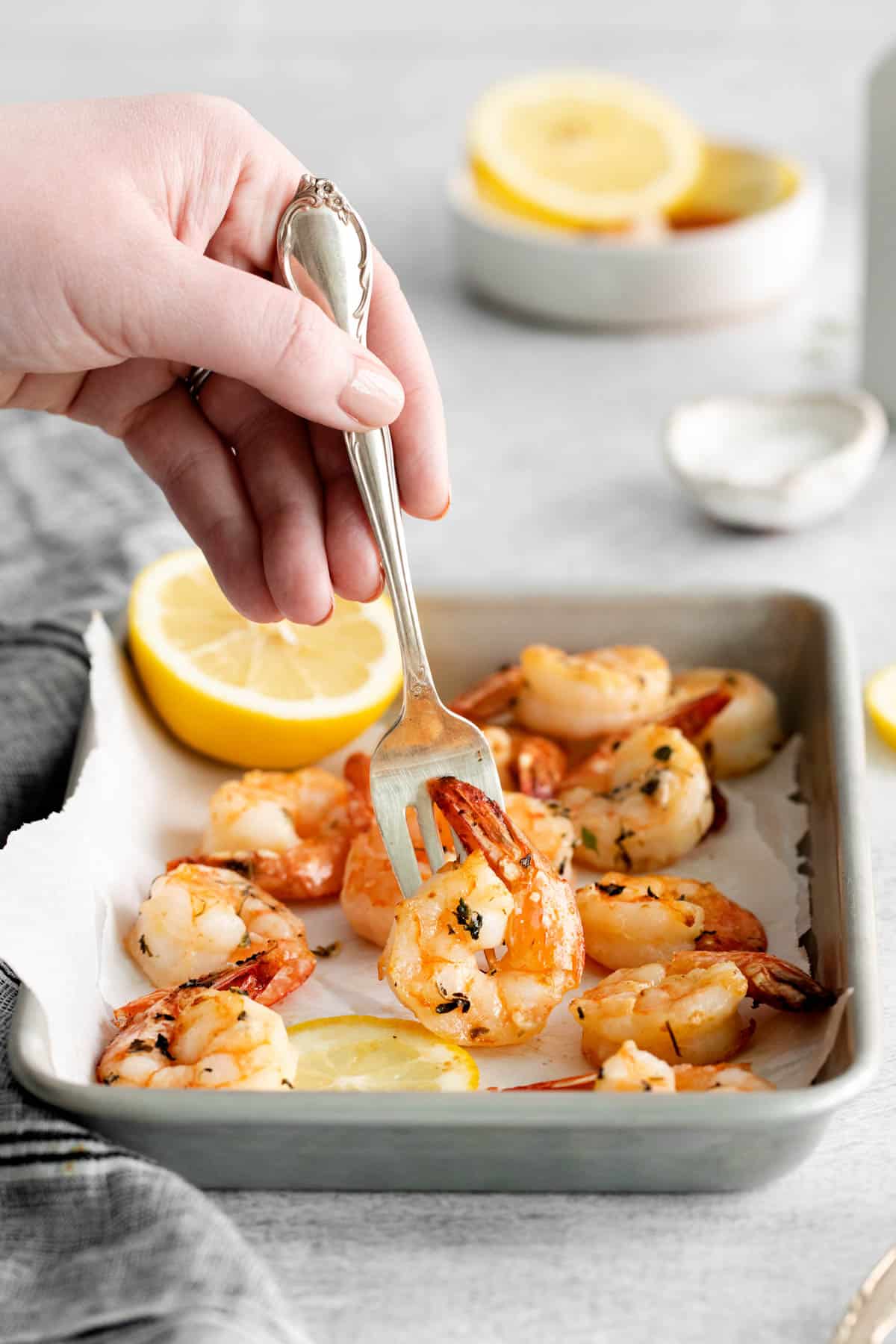 A hand holding a fork spearing a piece of air fryer shrimp with garlic herb butter.