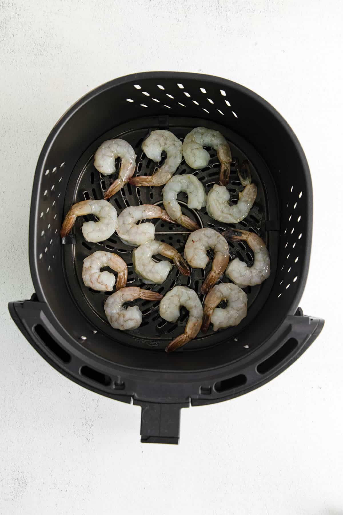 An air fryer basket with raw shrimp in it.