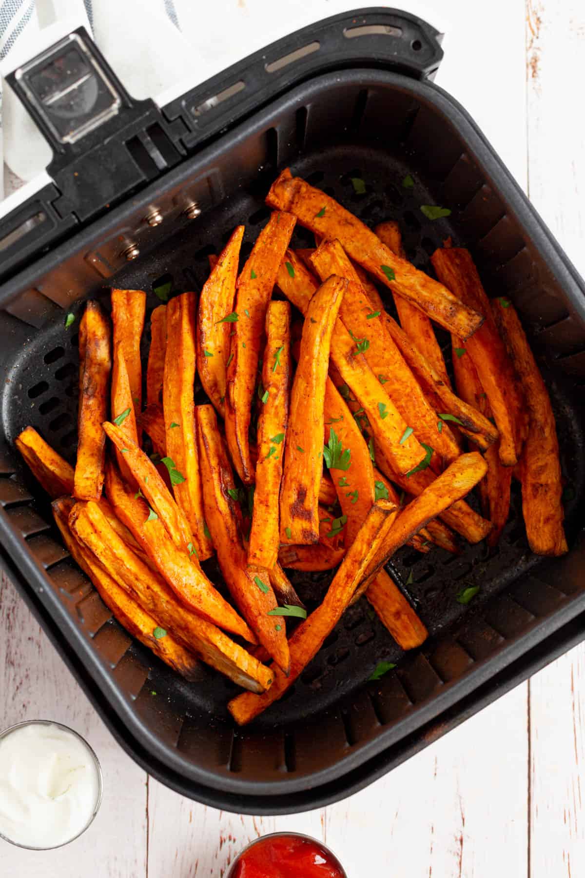 Overhead view of sweet potato fries in an air cooker, displaying more of the air cooker as well as dipping sauces surrounding it in individual bowls. 