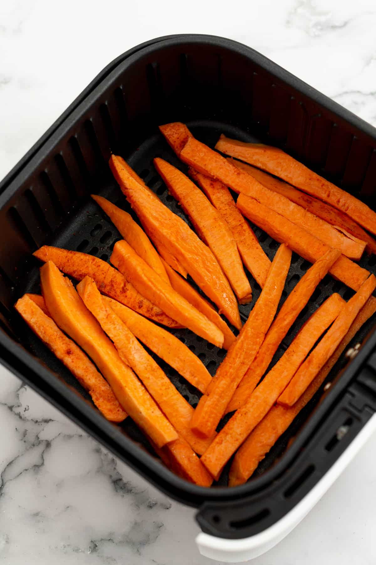 Cut sweet potatoes arranged in an air fryer before cooking. 