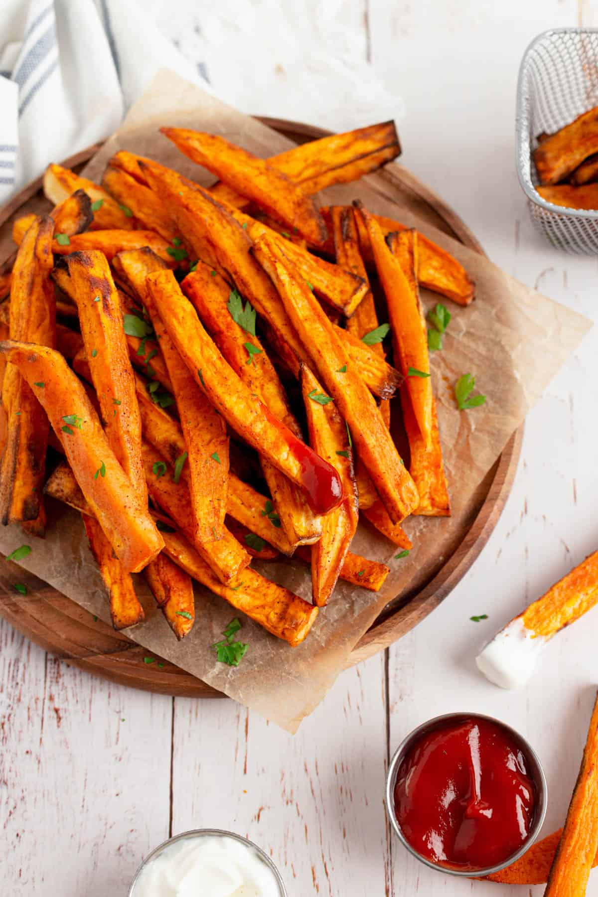 Close up view of cooked sweet potato fries, garnished with chopped cilantro and showing a few fries dipped in sauces. 