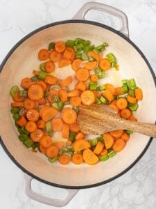 Overhead view of wooden spoon stirring vegetables in Dutch oven