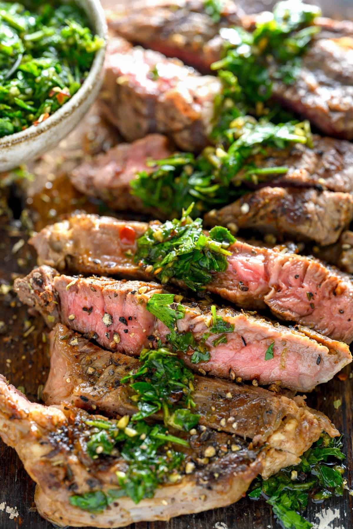 A sliced medium-rare steak with chimichurri sauce drizzled on top.