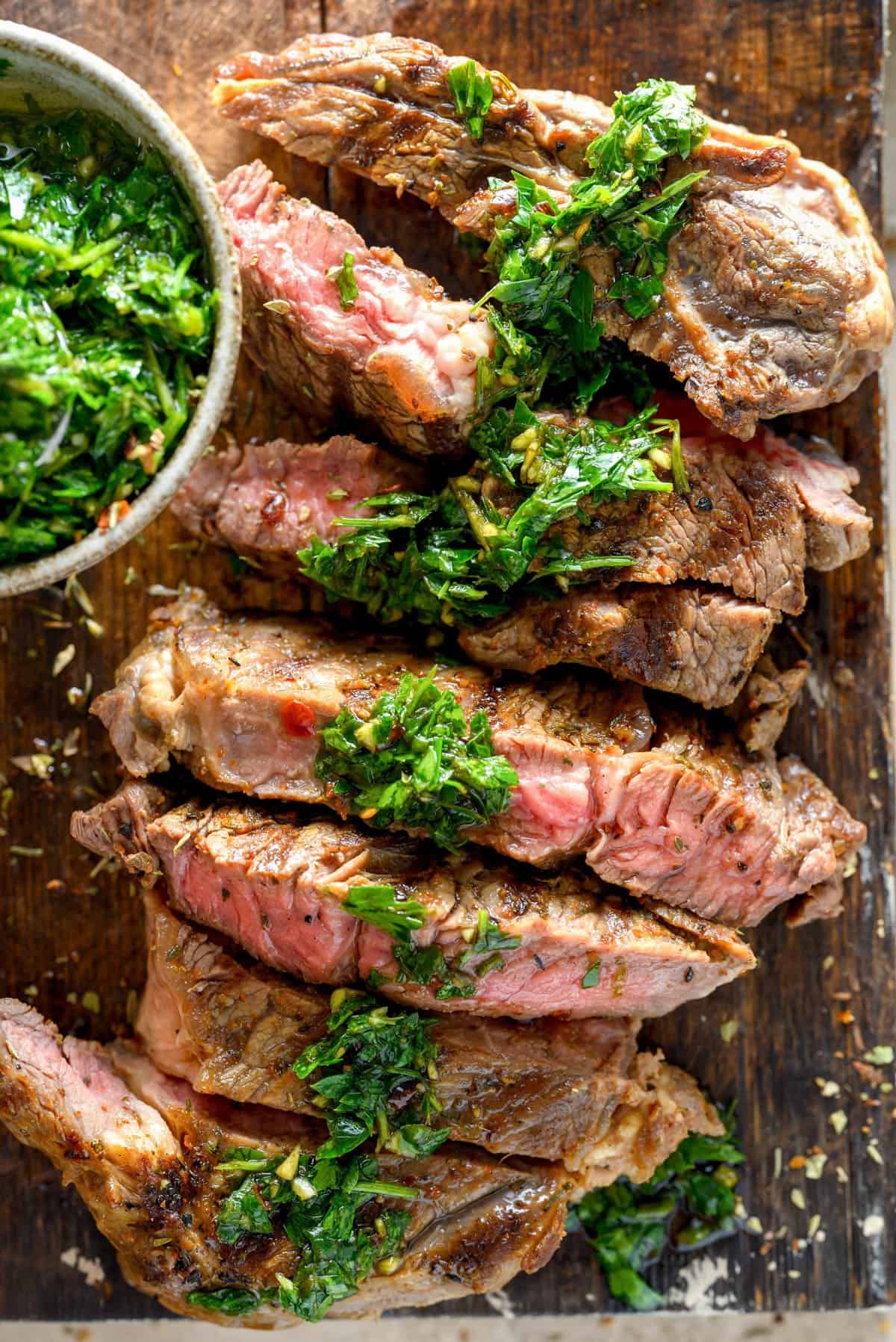 A sliced medium-rare steak with chimichurri sauce drizzled on top.
