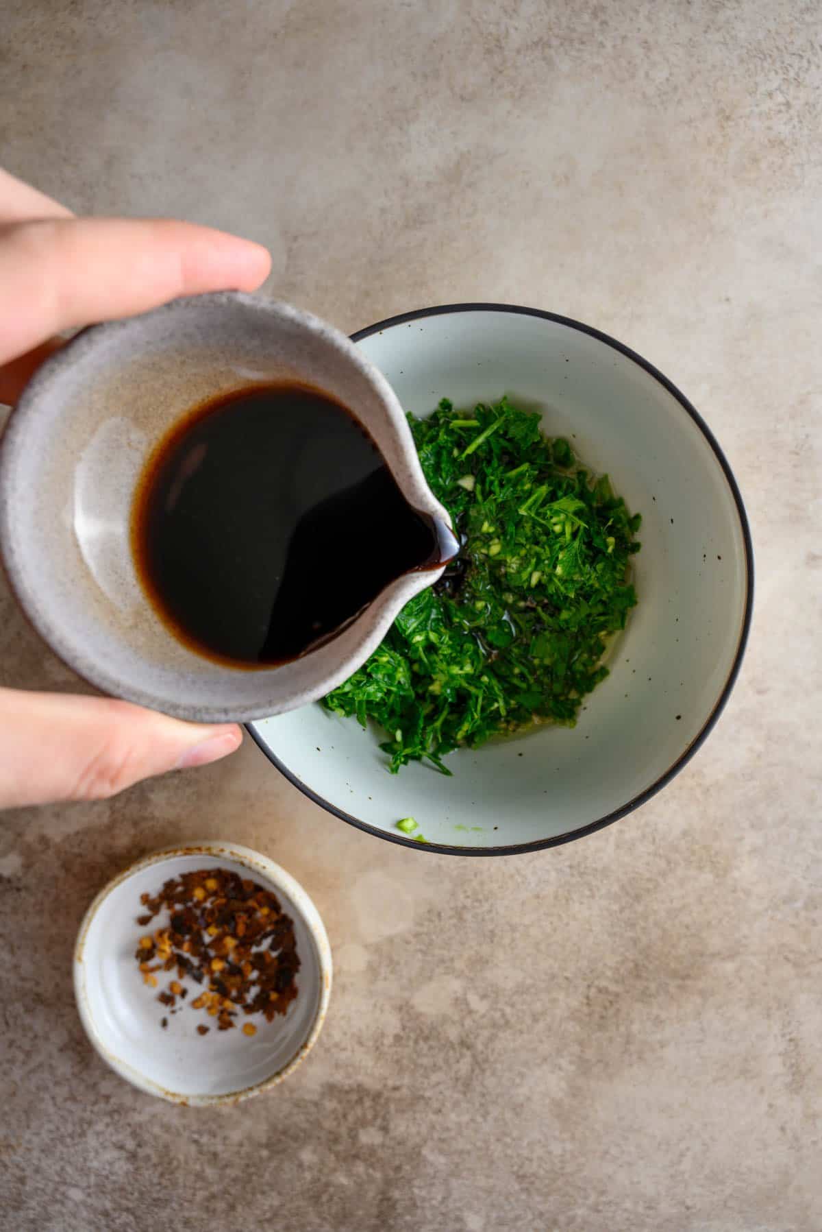 Adding ingredients to a bowl to make a chimichurri sauce.