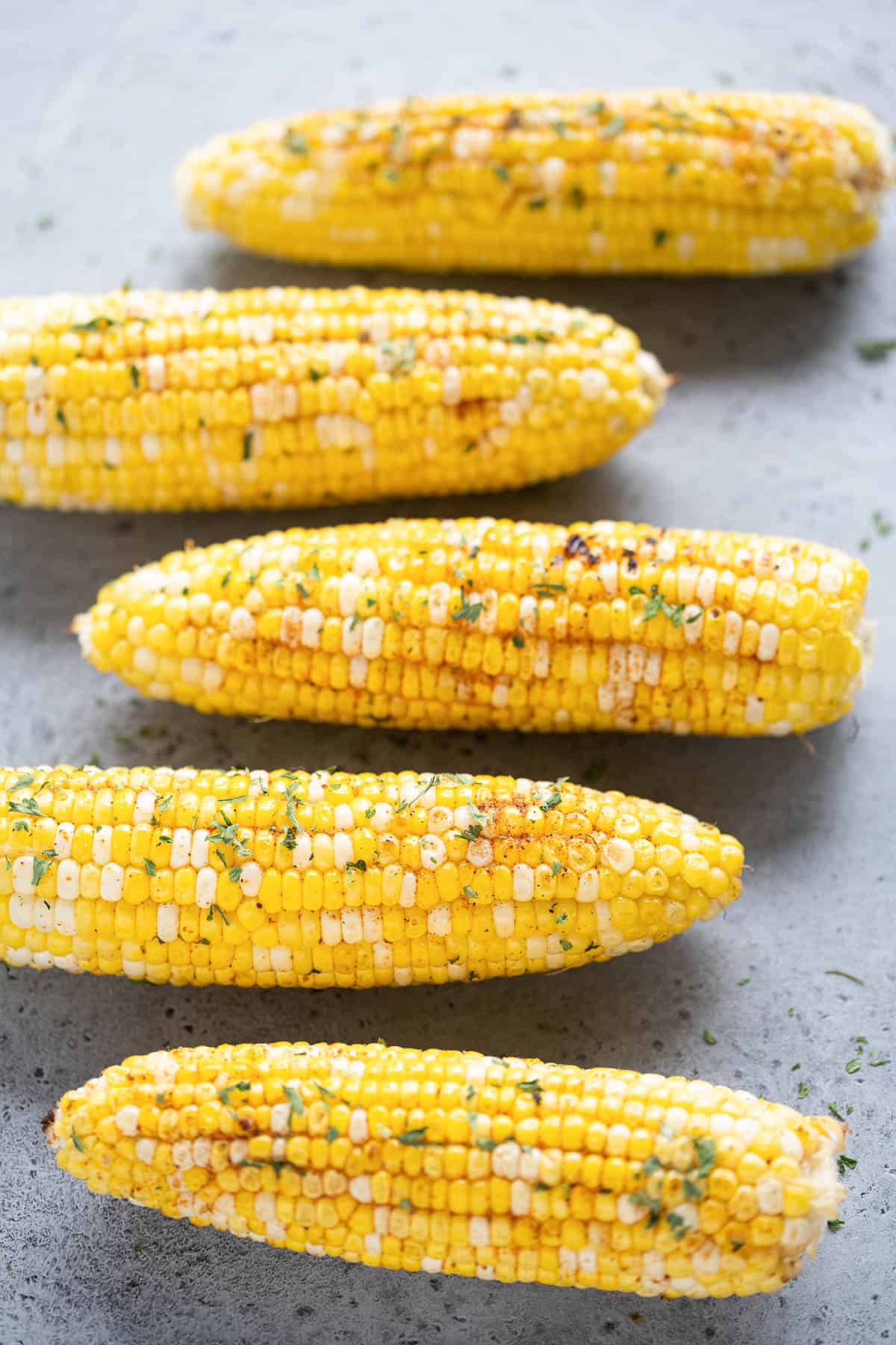 Five ears of grilled corn on the cob arranged in a row.