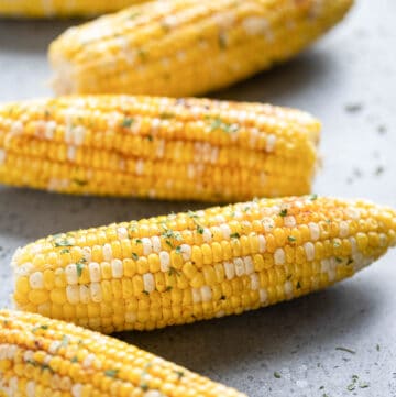 Five ears of grilled corn on the cob on a grey surface.