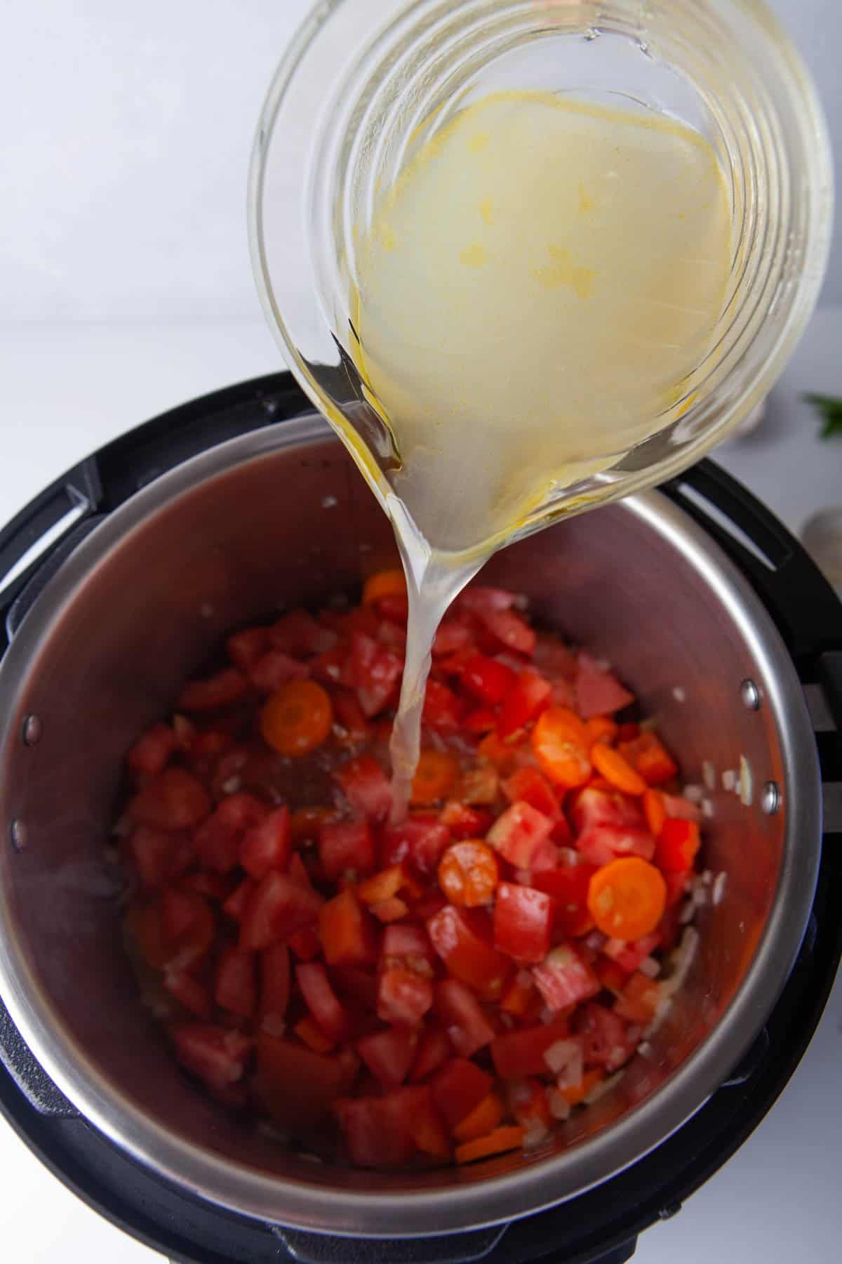 Adding chicken broth to diced tomatoes, carrots and onions in an Instant Pot.