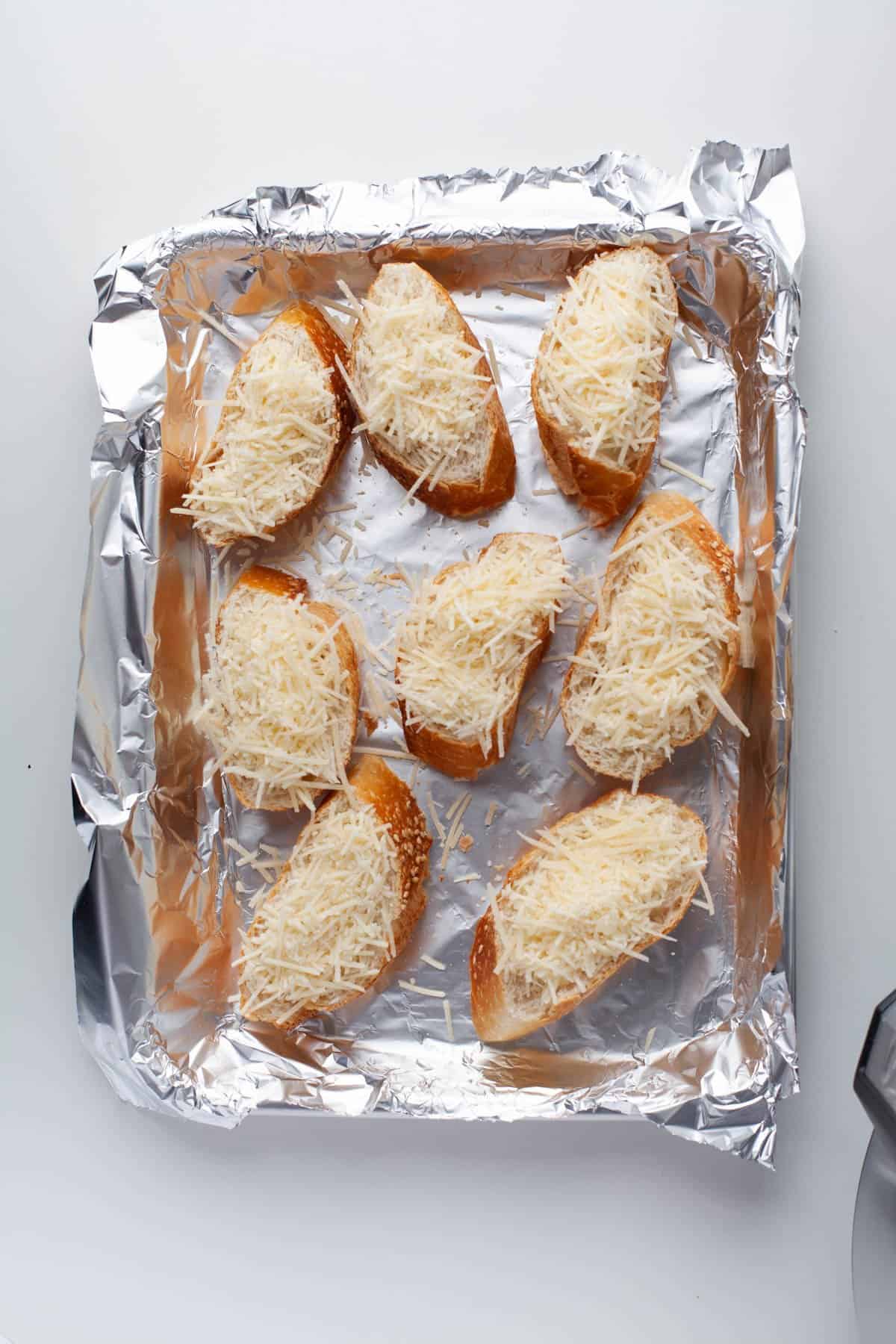Cheese sprinkled on slices of toast on a baking sheet lined with foil