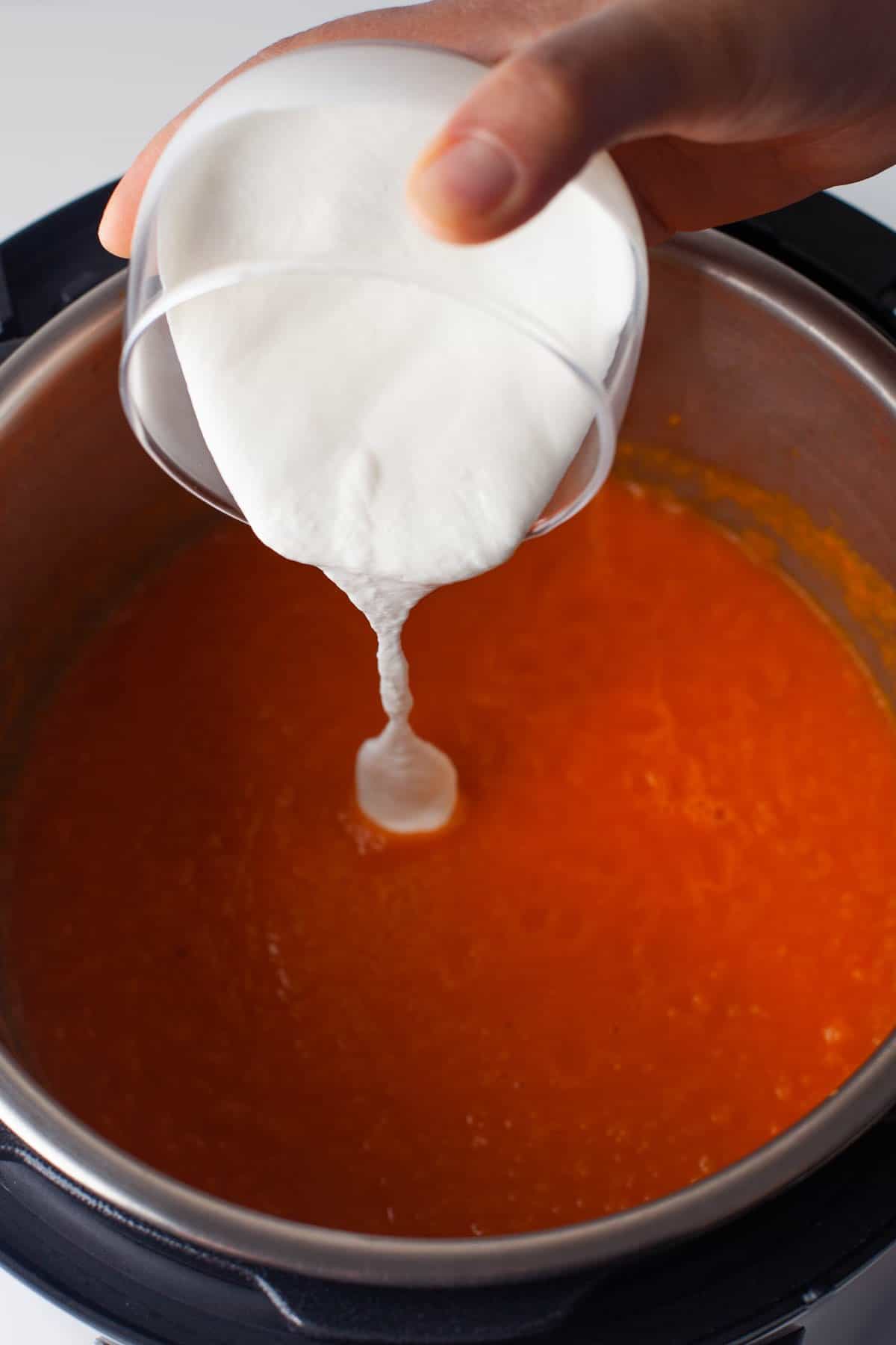 Adding cream to homemade tomato soup in the Instant Pot.