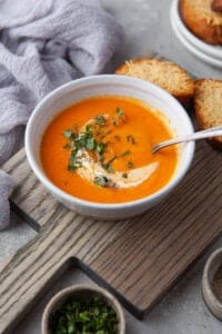 A bowl of homemade tomato soup with a swirl of cream and herbs sprinkled on top.