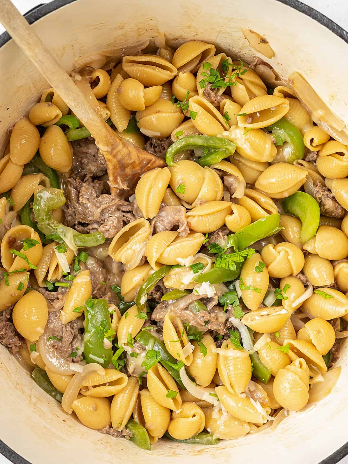 Philly cheesesteak pasta in Dutch oven with wooden spoon