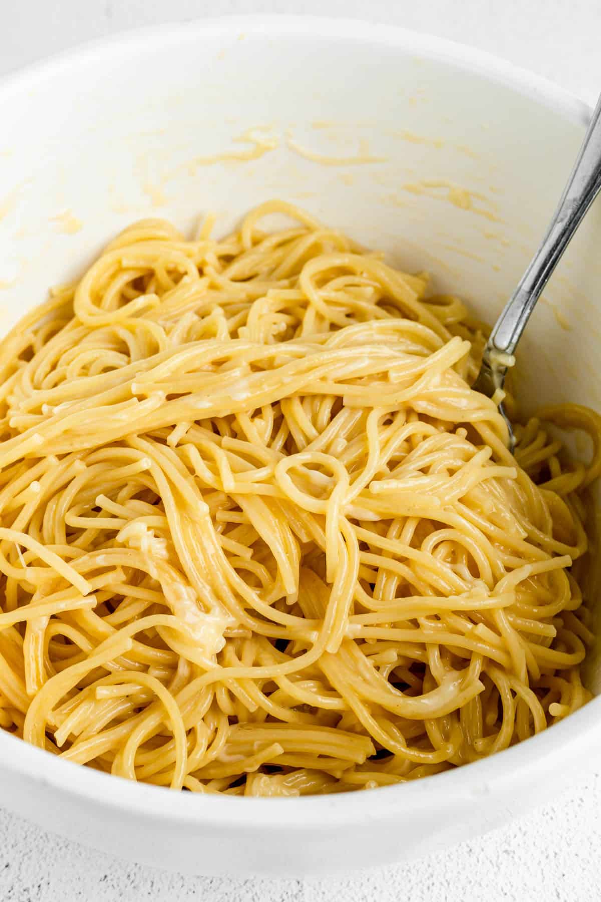 Stirring cooked spaghetti noodles with a beaten egg to make spaghetti pie.
