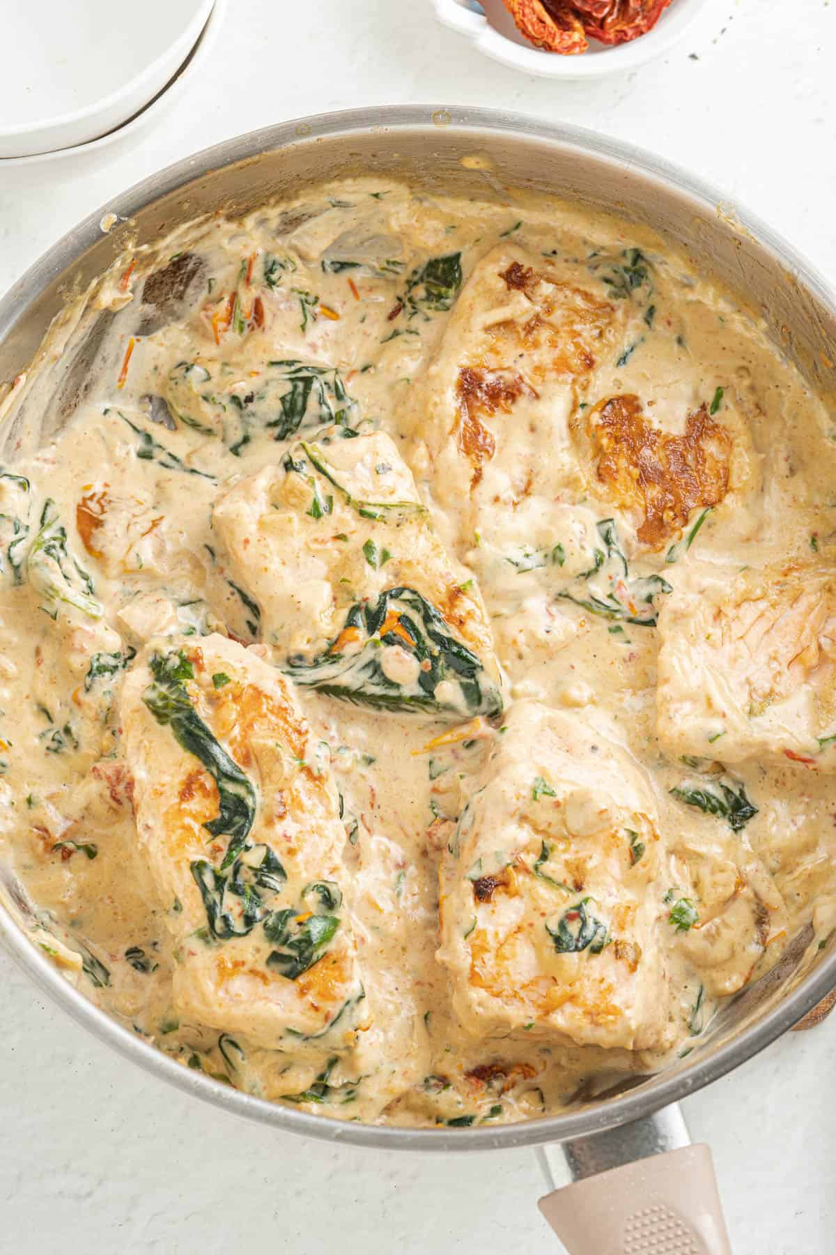An overhead image of a saucepan filled with creamy Tuscan salmon fillets in a sauce made with spinach and sundried tomatoes.