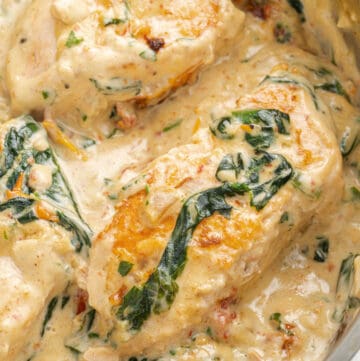 A close image of salmon fillets cooked in a creamy Tuscan sauce in a pan.