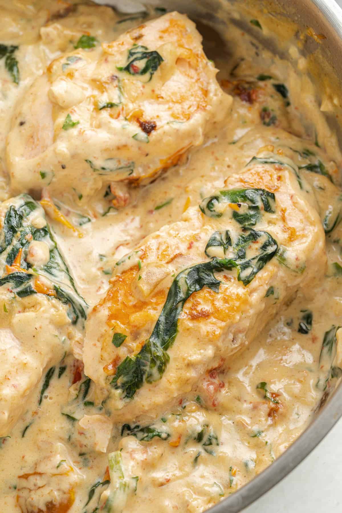 A close image of salmon fillets cooked in a creamy Tuscan sauce in a pan.