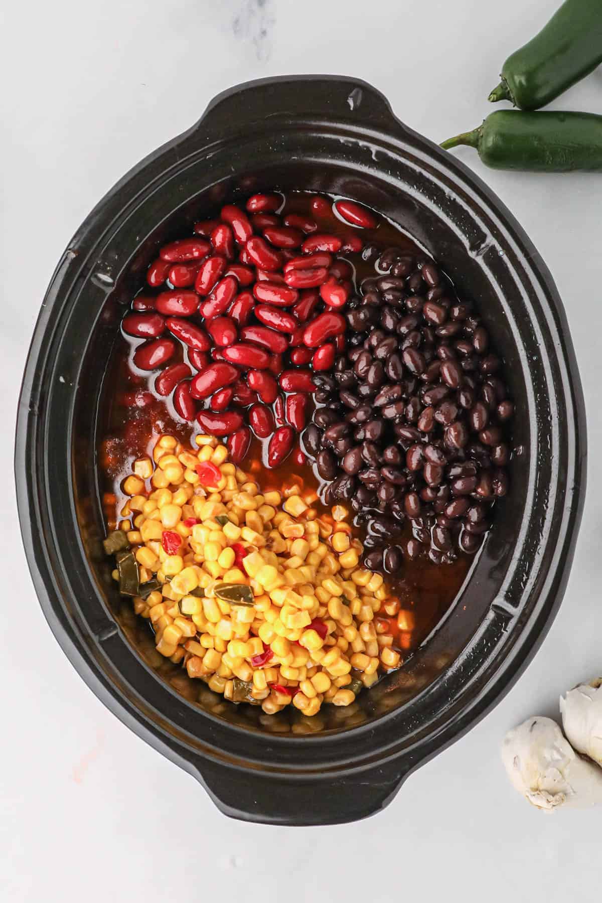Red kidney beans, yellow corn with spices, and black beans in a slow cooker.