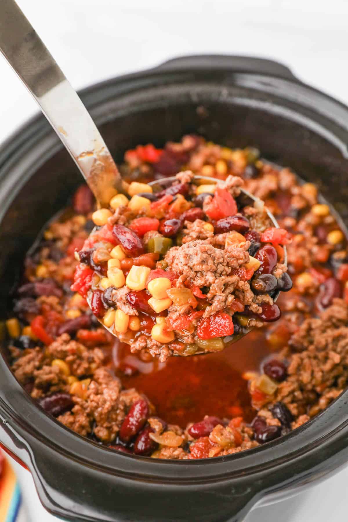 A ladle lifting a scoop of taco soup from a crock pot.