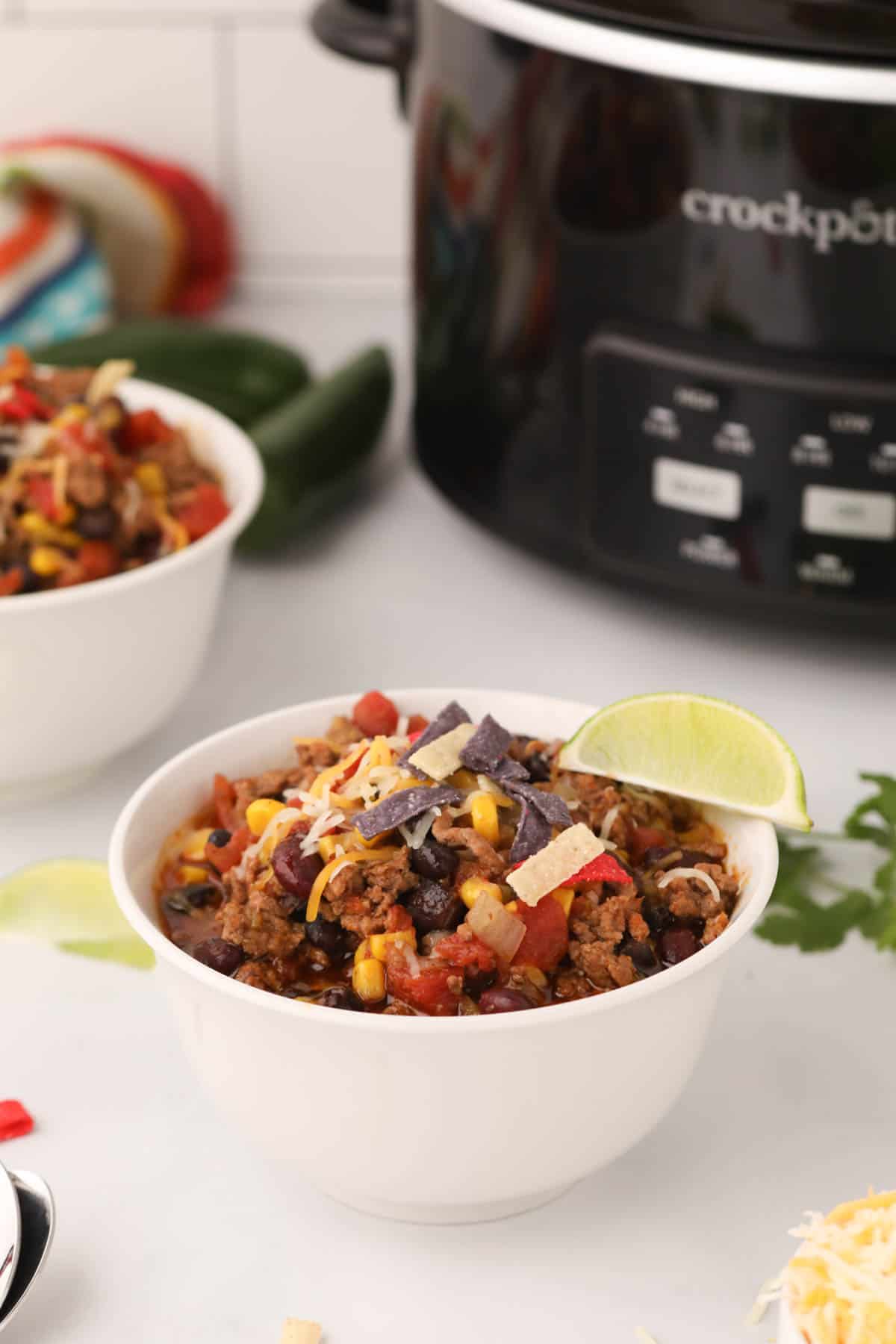 A bowl of taco soup in front of a crock pot.