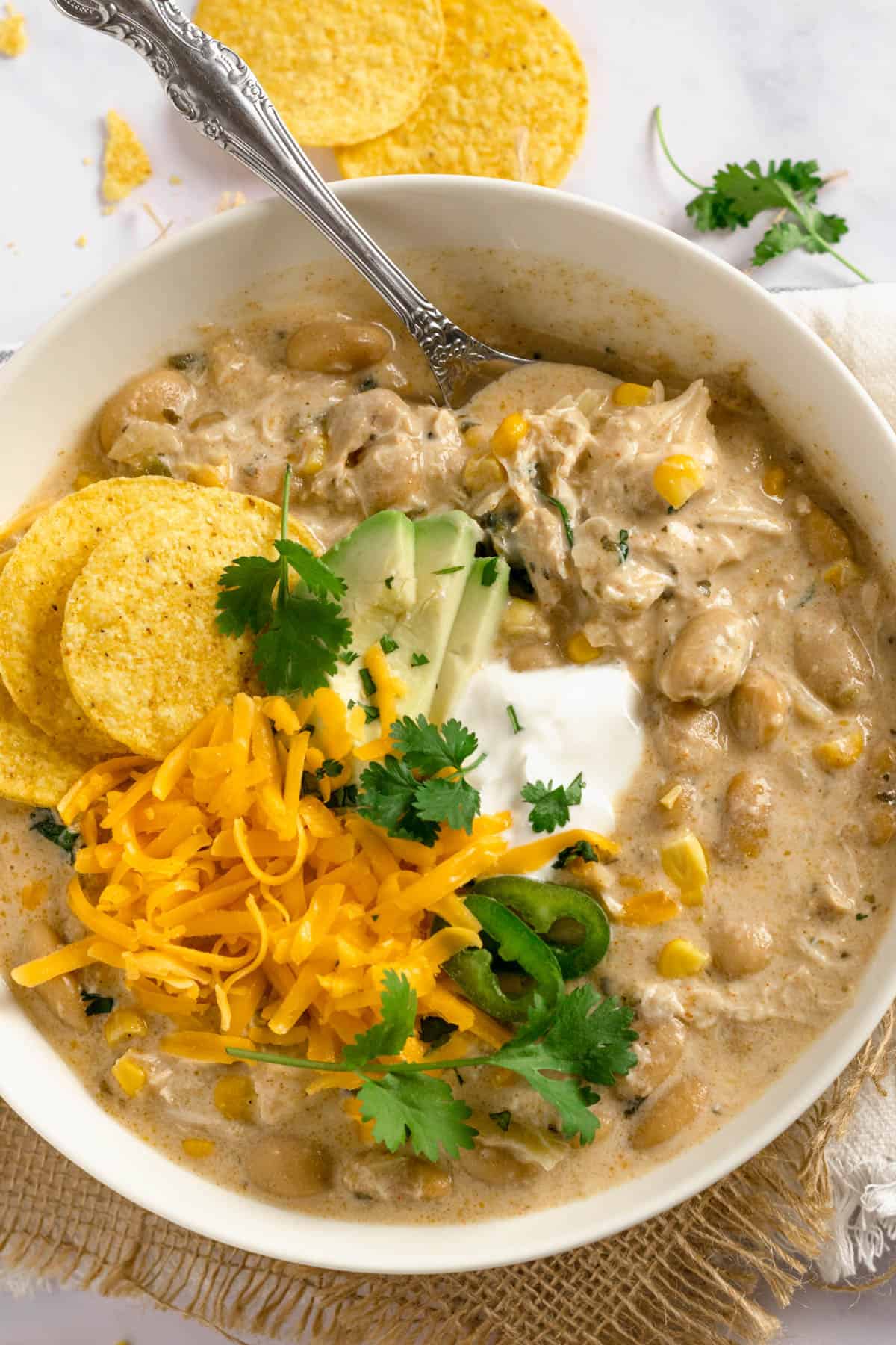 A bowl of crock pot white chicken chili with sour cream, cheese, cilantro, and avocado toppings.