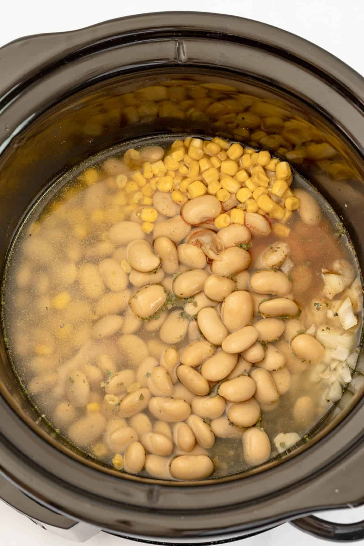 Adding white beans and corn to a slow cooker with chicken broth.