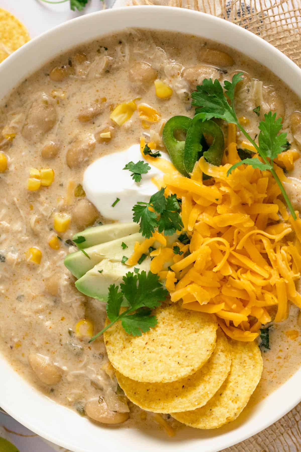 An overhead image of creamy white chicken chili with corn chips, avocado, sour cream and cheese in a bowl.