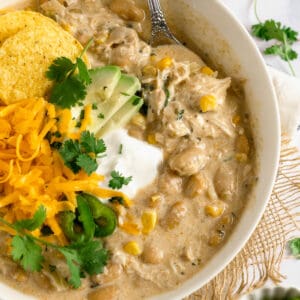 A bowl of crock pot white chicken chili with sour cream, cheese, cilantro, and avocado toppings.