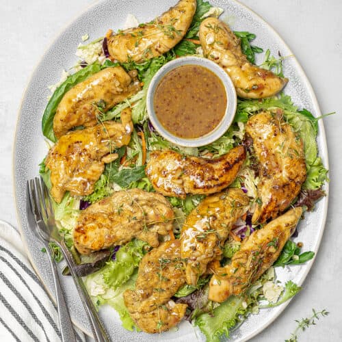 Platter of honey mustard chicken on bed of greens with extra sauce