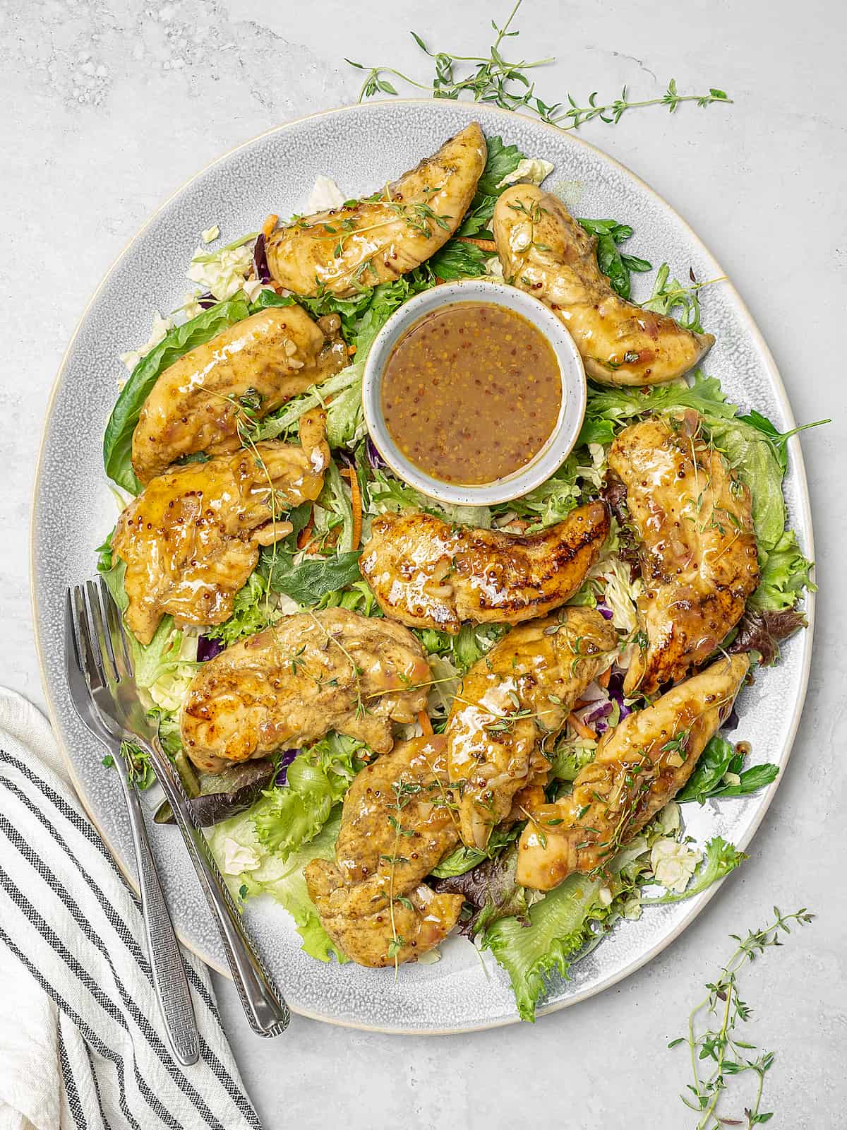 Platter of honey mustard chicken on bed of greens with extra sauce