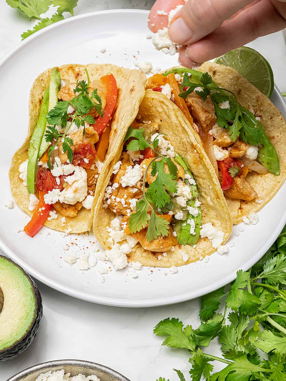 Chicken fajitas on plate, with hand sprinkling queso fresco on top