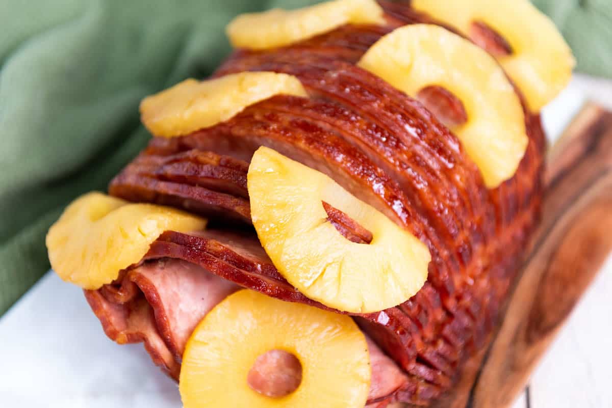 A spiral sliced ham with pineapple rings tucked between slices next to a green cloth napkin.