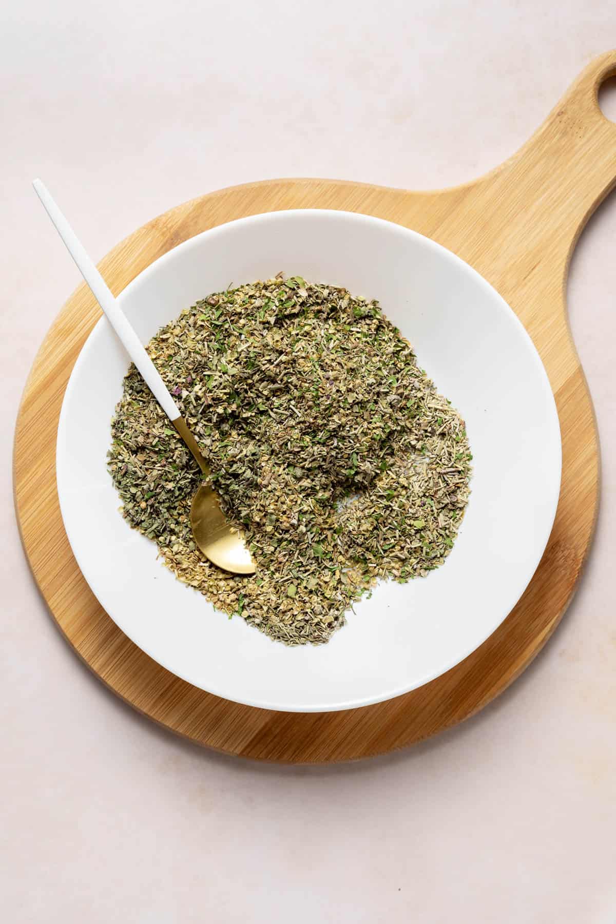Herbs mixed together in a shallow white bowl with a spoon.