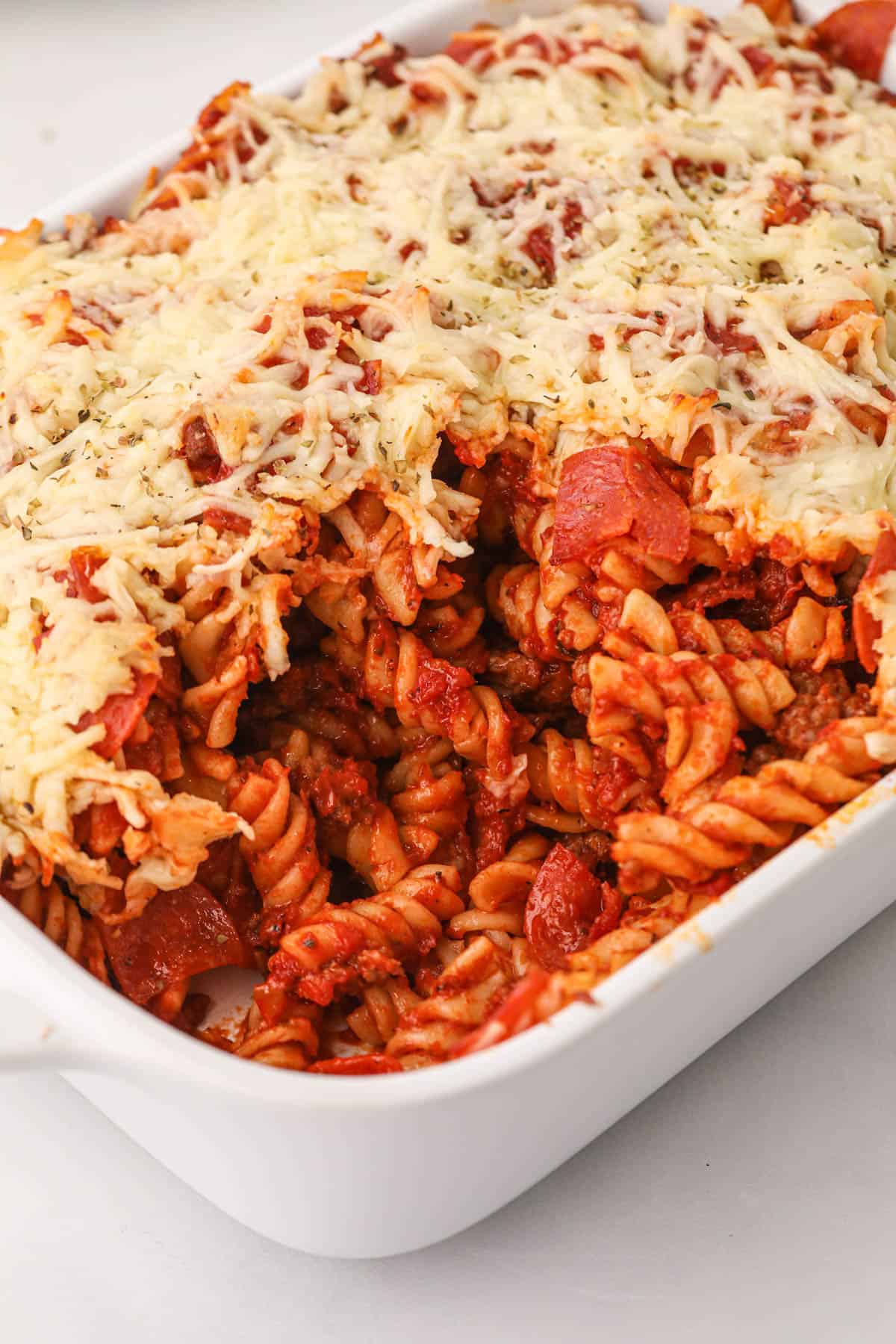 A white casserole dish filled with pizza pasta with a scoop taken out of it.