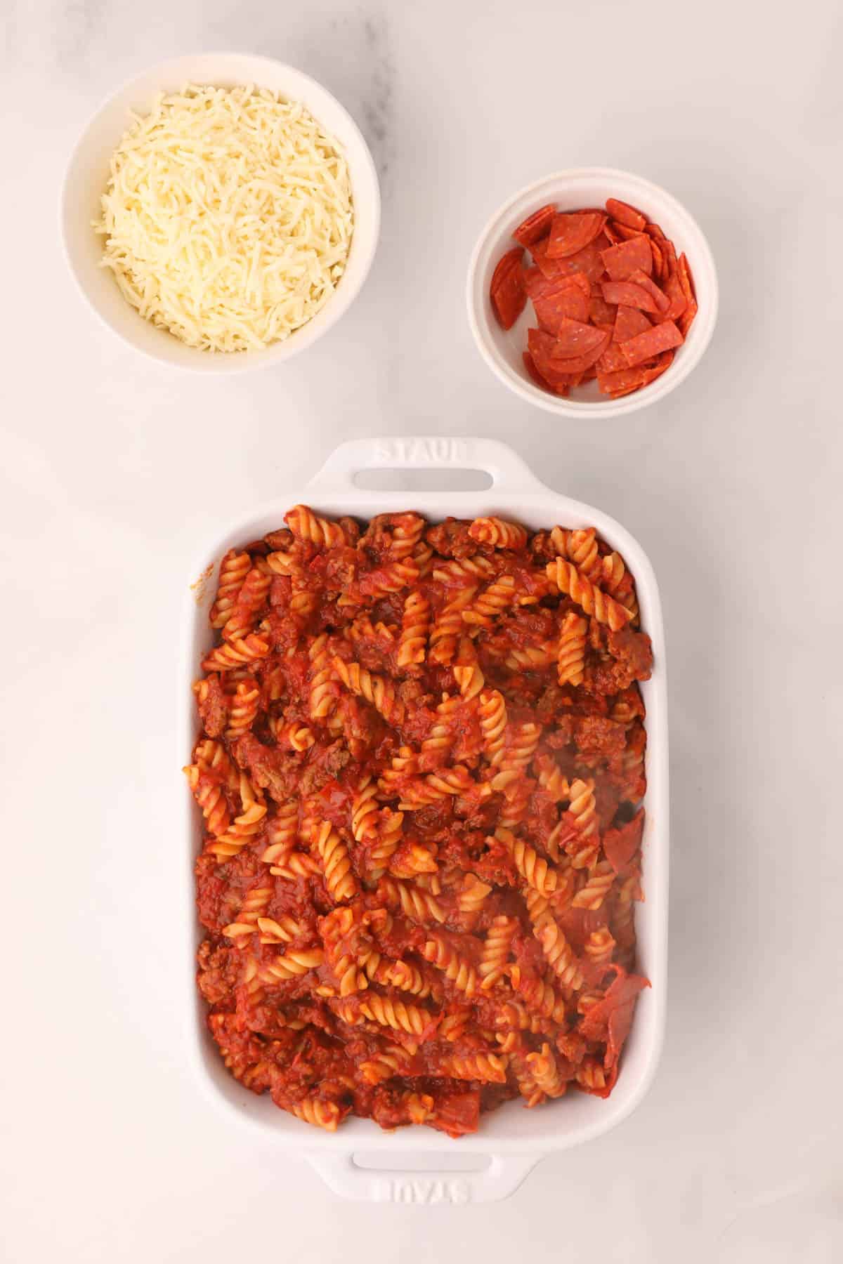 A white casserole dish filled with pasta tossed with meaty Italian sausage marinara sauce.
