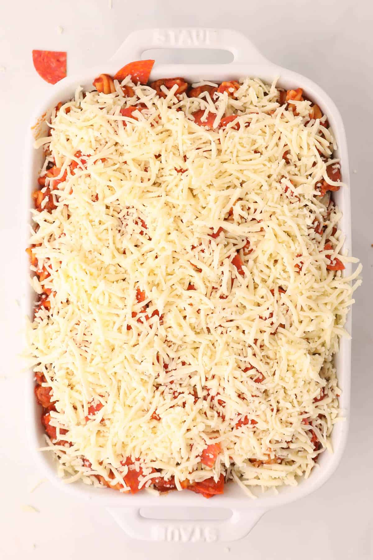 Pizza casserole topped with shredded mozzarella cheese before being baked in the oven.