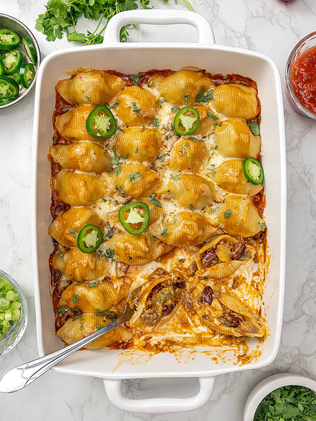 Baking dish of taco stuffed shells with serving spoon