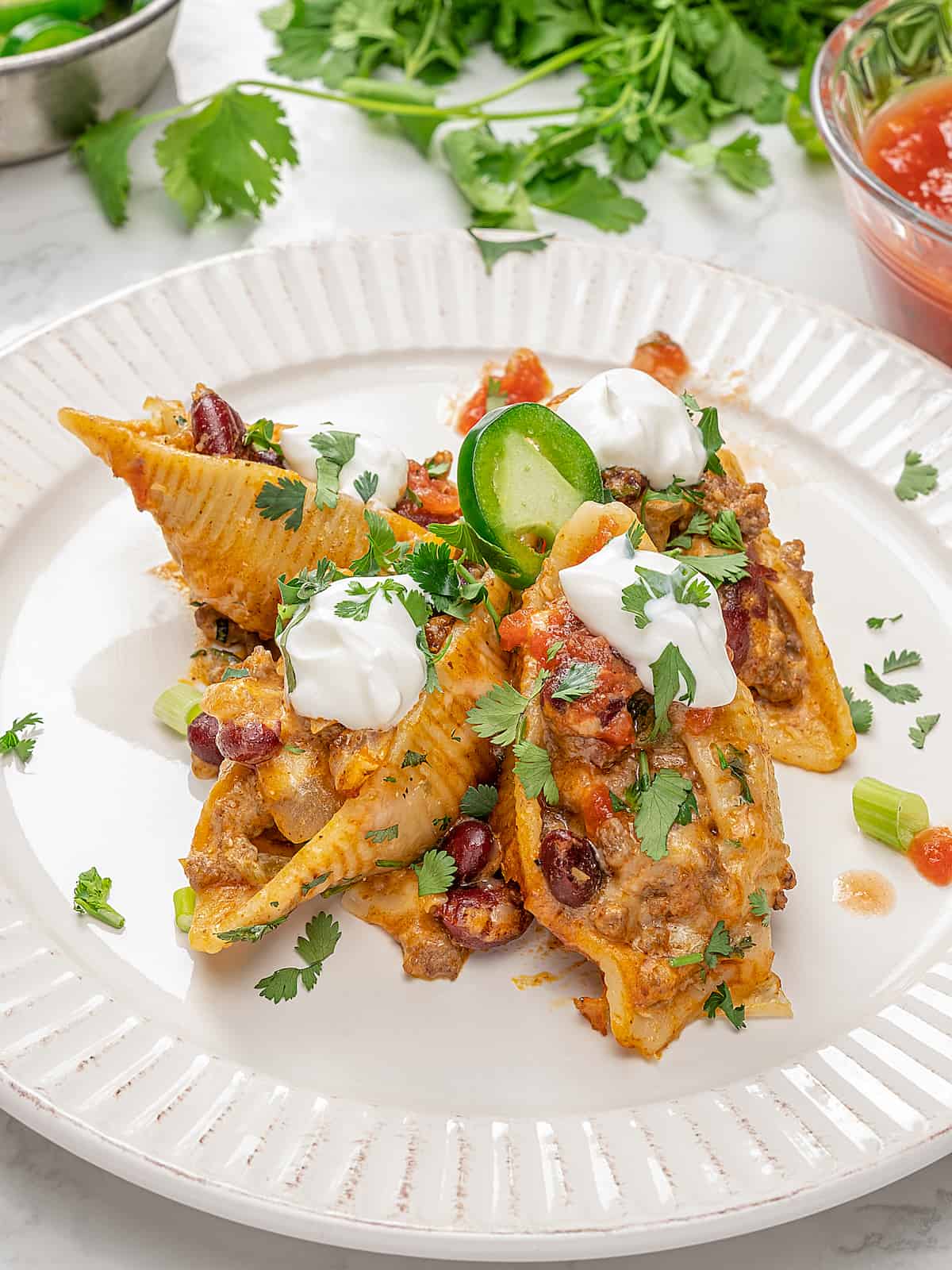 Taco stuffed shells on plate with sour cream and garnishes