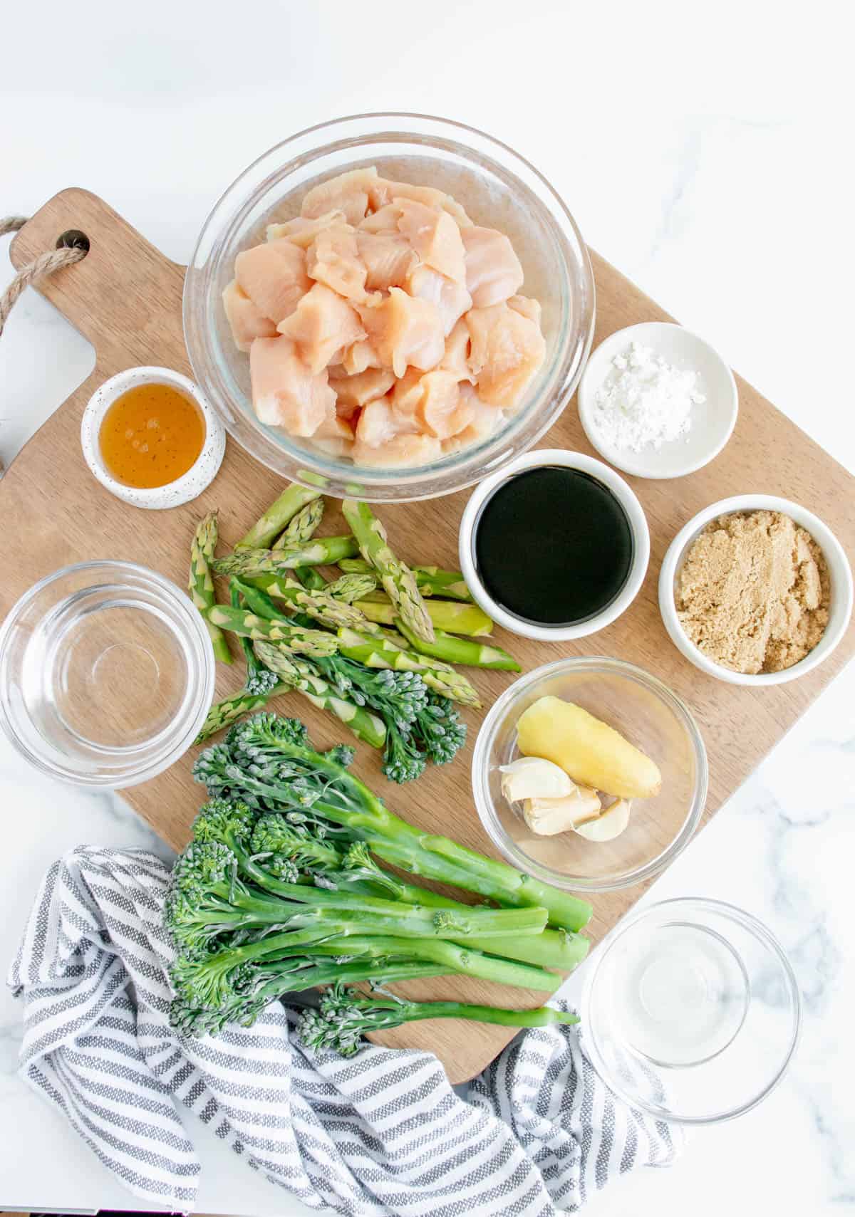 Ingredients for Teriyaki Chicken with asparagus and broccolini, displayed in separate bowls on a wooden cutting board