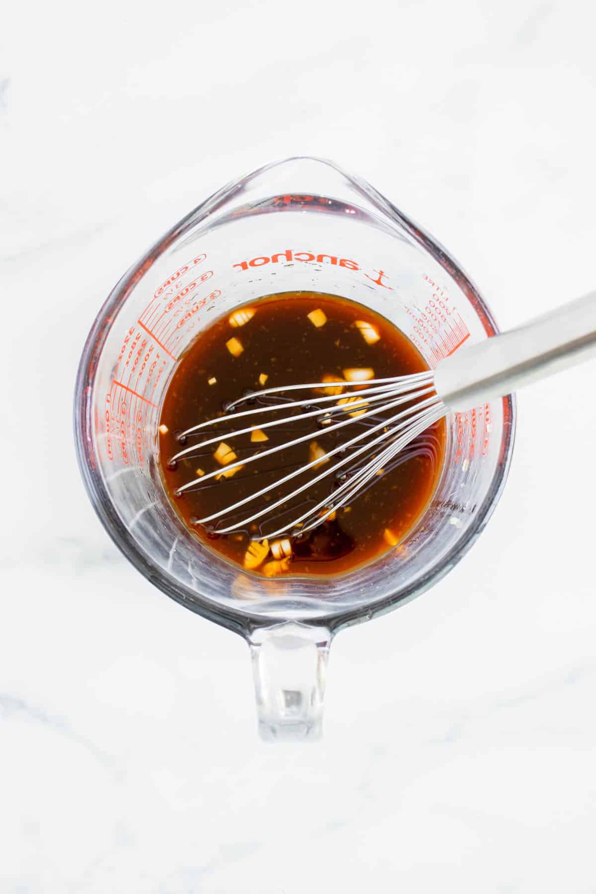 Overhead image of sauce in a glass measuring cup with a metal wisk