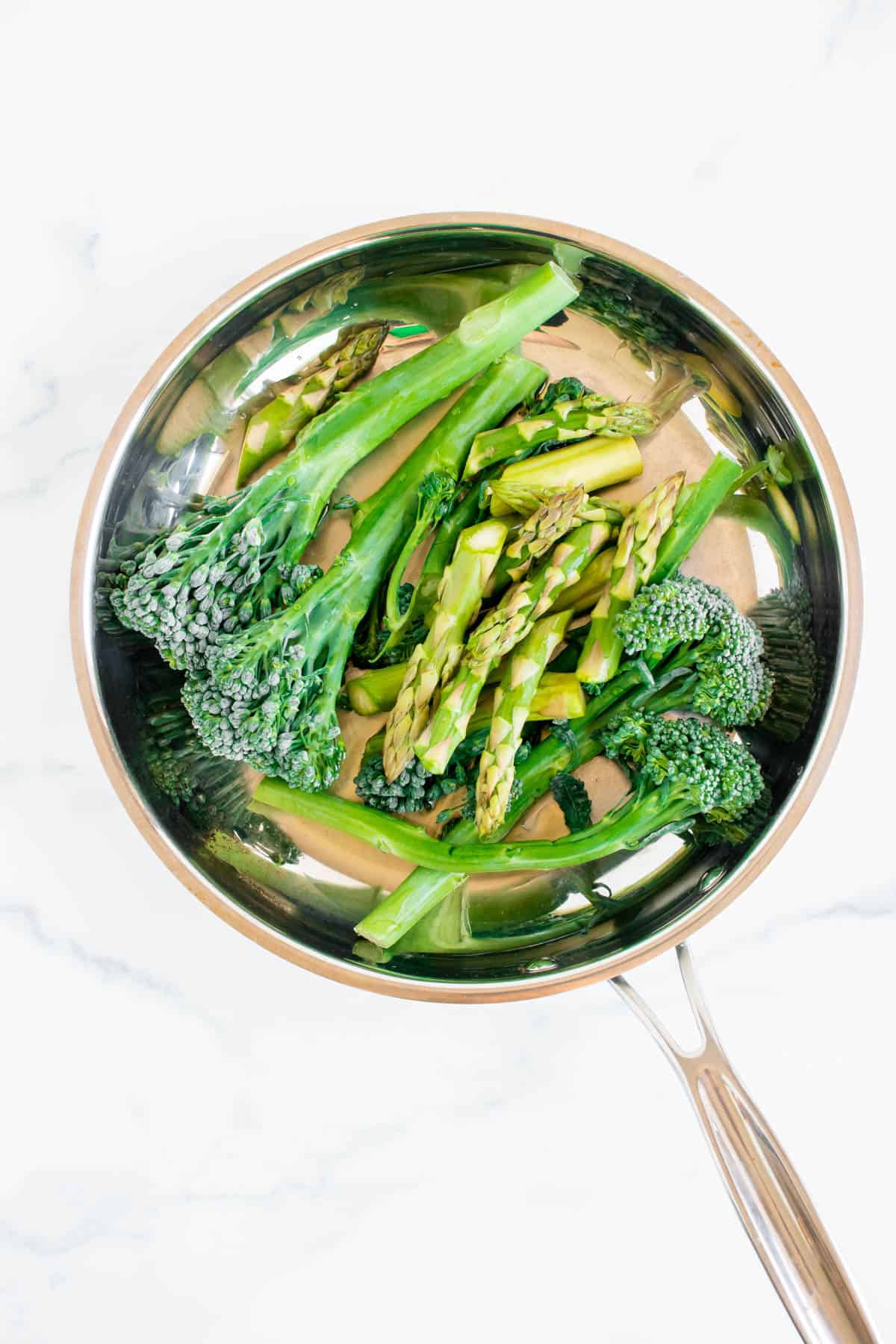 Raw broccolini and asparagus are in a silver skillet