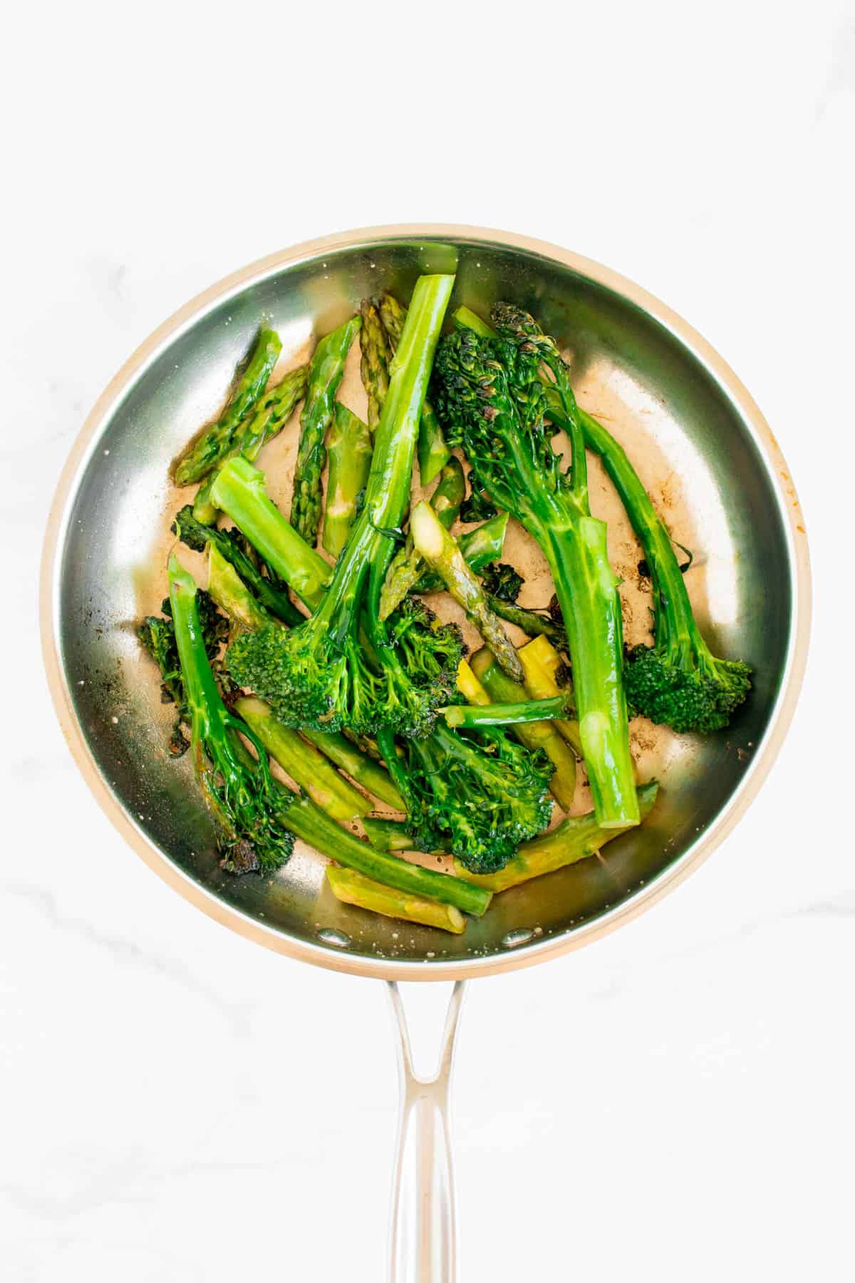 Asparagus and broccolini are in a silver skillet, and have been cooked.