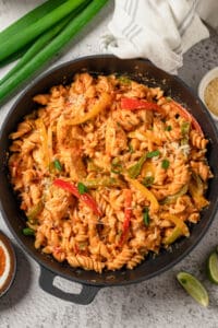 An overhead image of chicken fajita pasta with red and yellow peppers in a large skillet.
