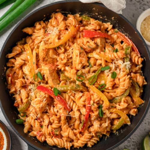 An overhead image of chicken fajita pasta with red and yellow peppers in a large skillet.