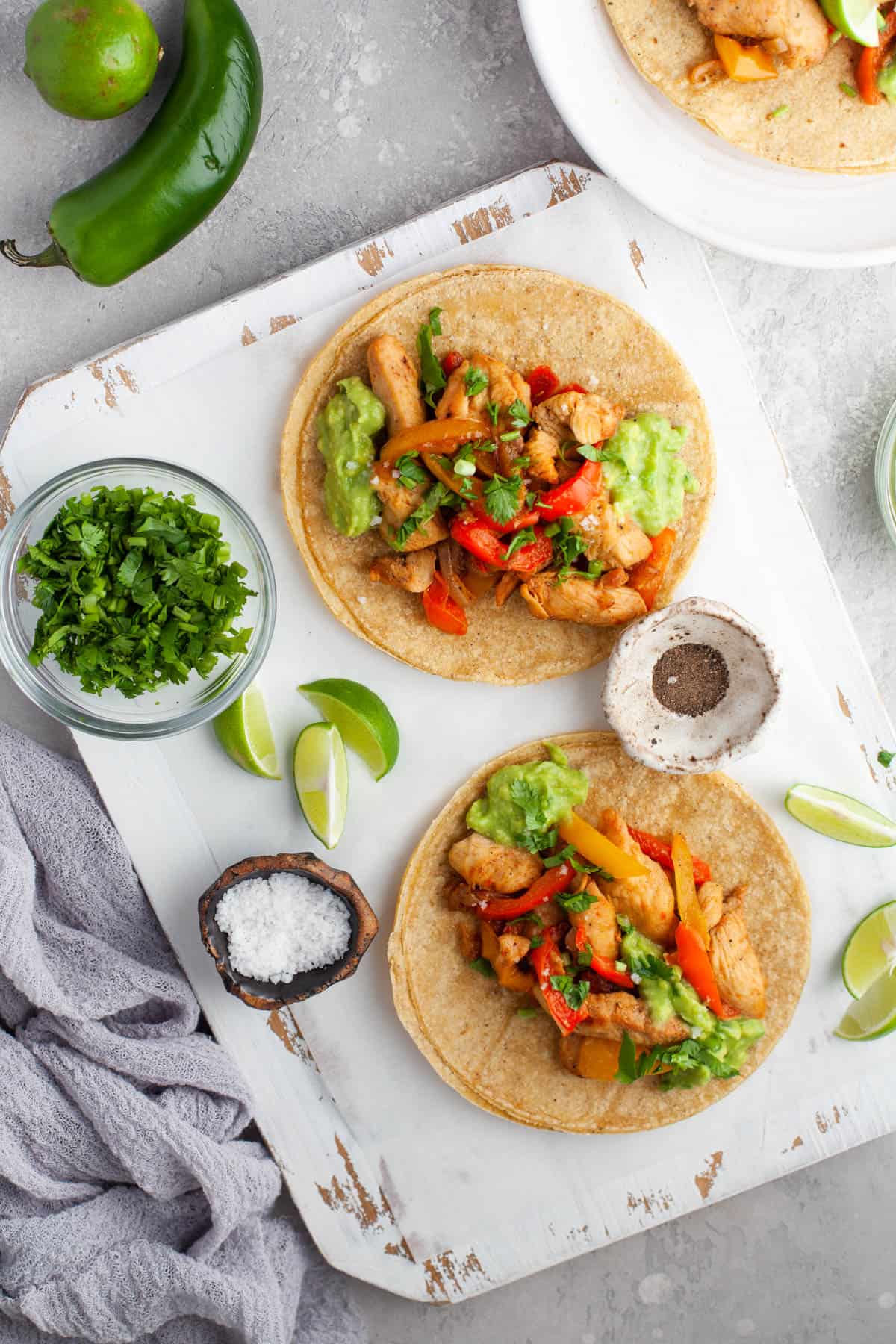 Chicken Fajitas on corn tortillas next to lime wedges, cilantro, and a jalapeno.