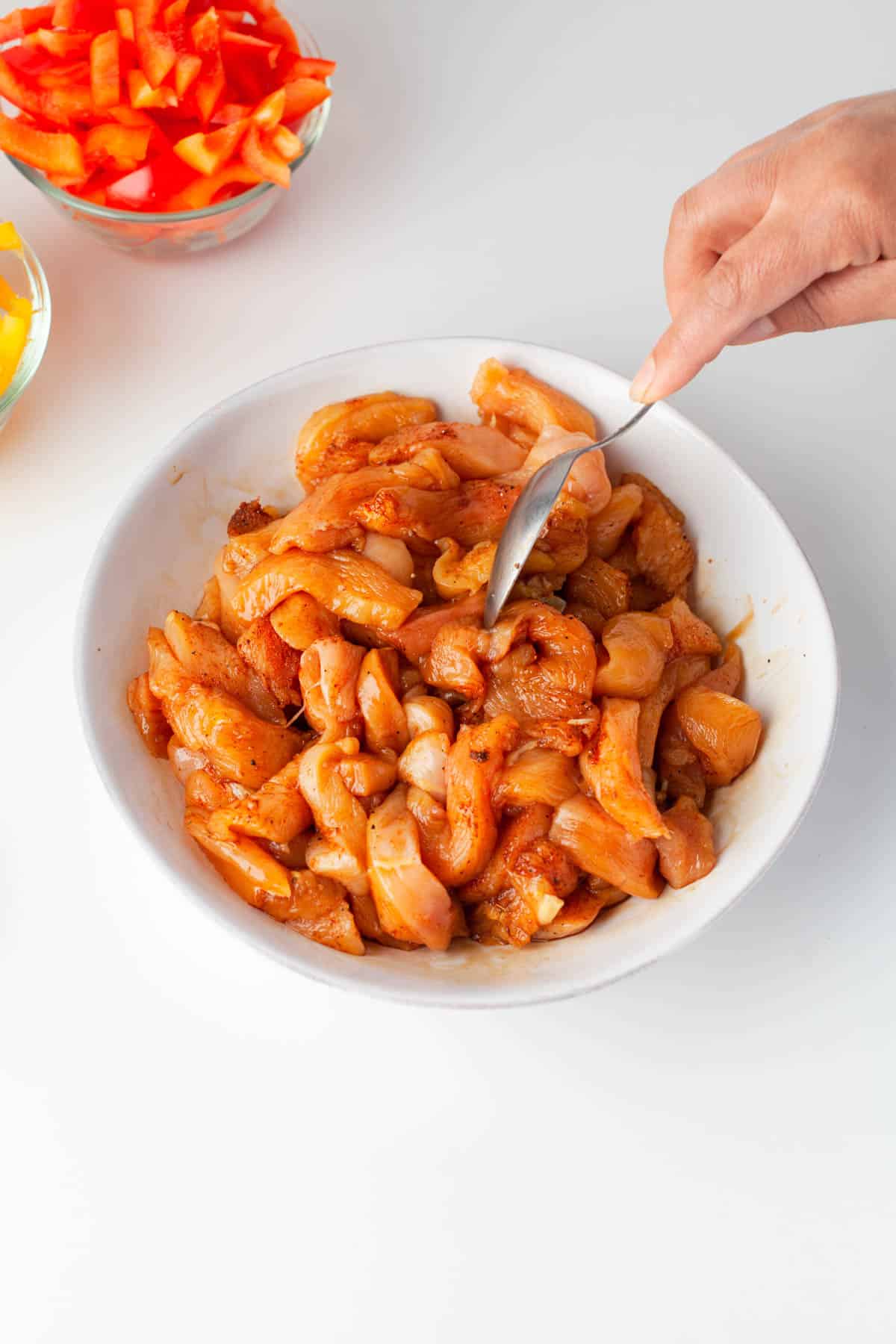 Stirring sliced chicken pieces in a bowl with fajita seasoning to evenly coat them in spices.