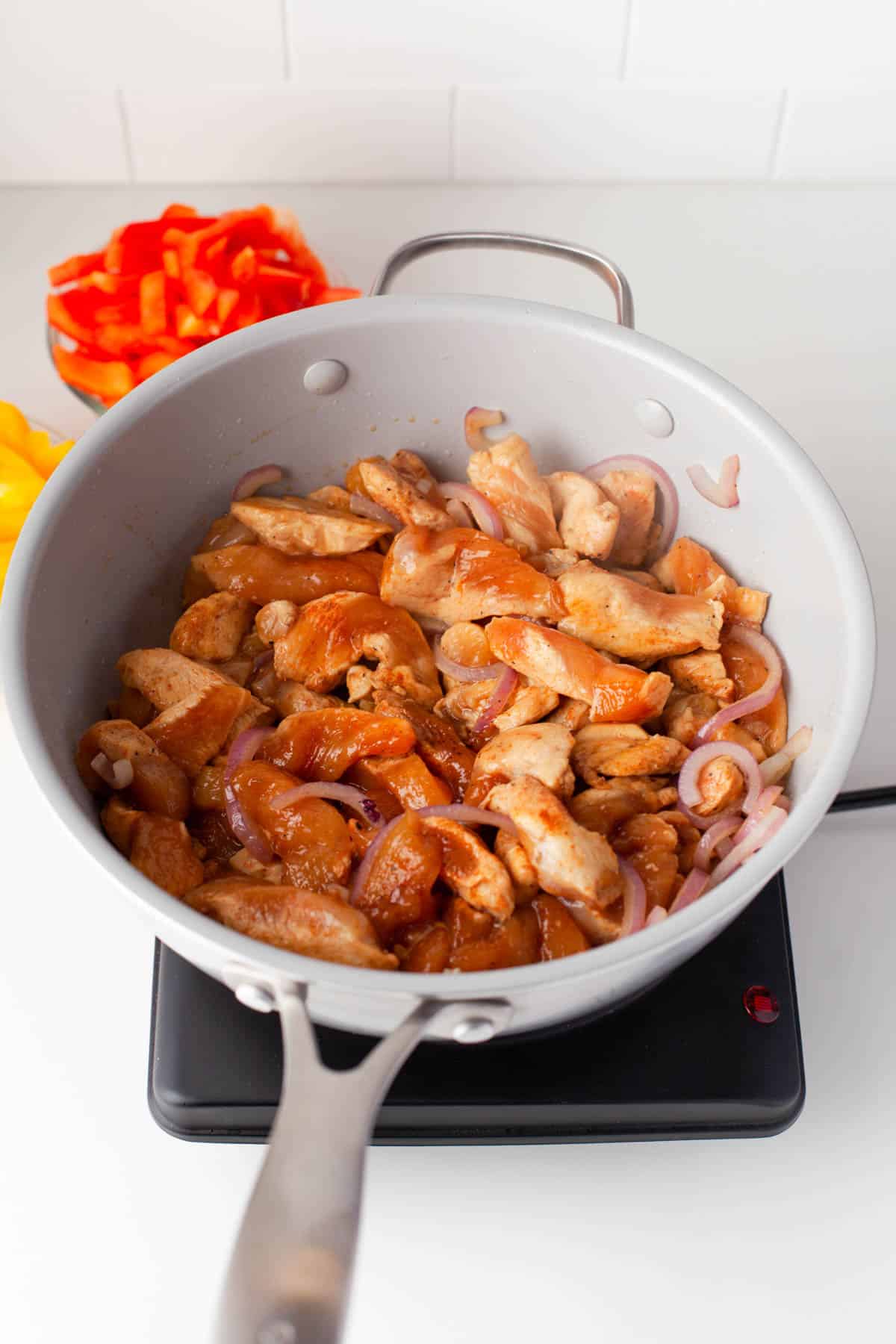 Cooking sliced chicken pieces in a large pan with fajita seasoning.