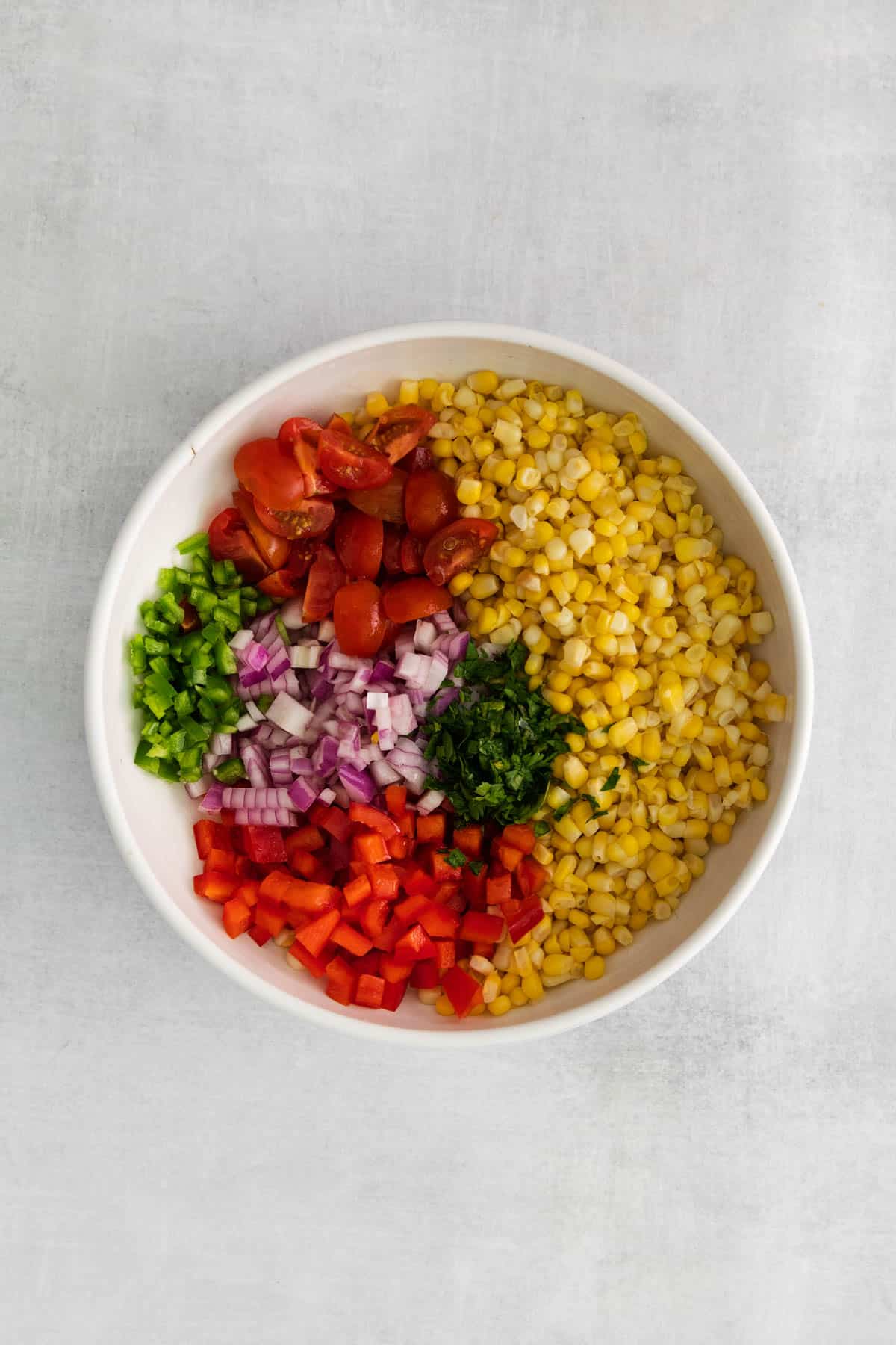 Corn kernels, tomatoes, onions, jalapeno, and other veggies in a large white bowl.