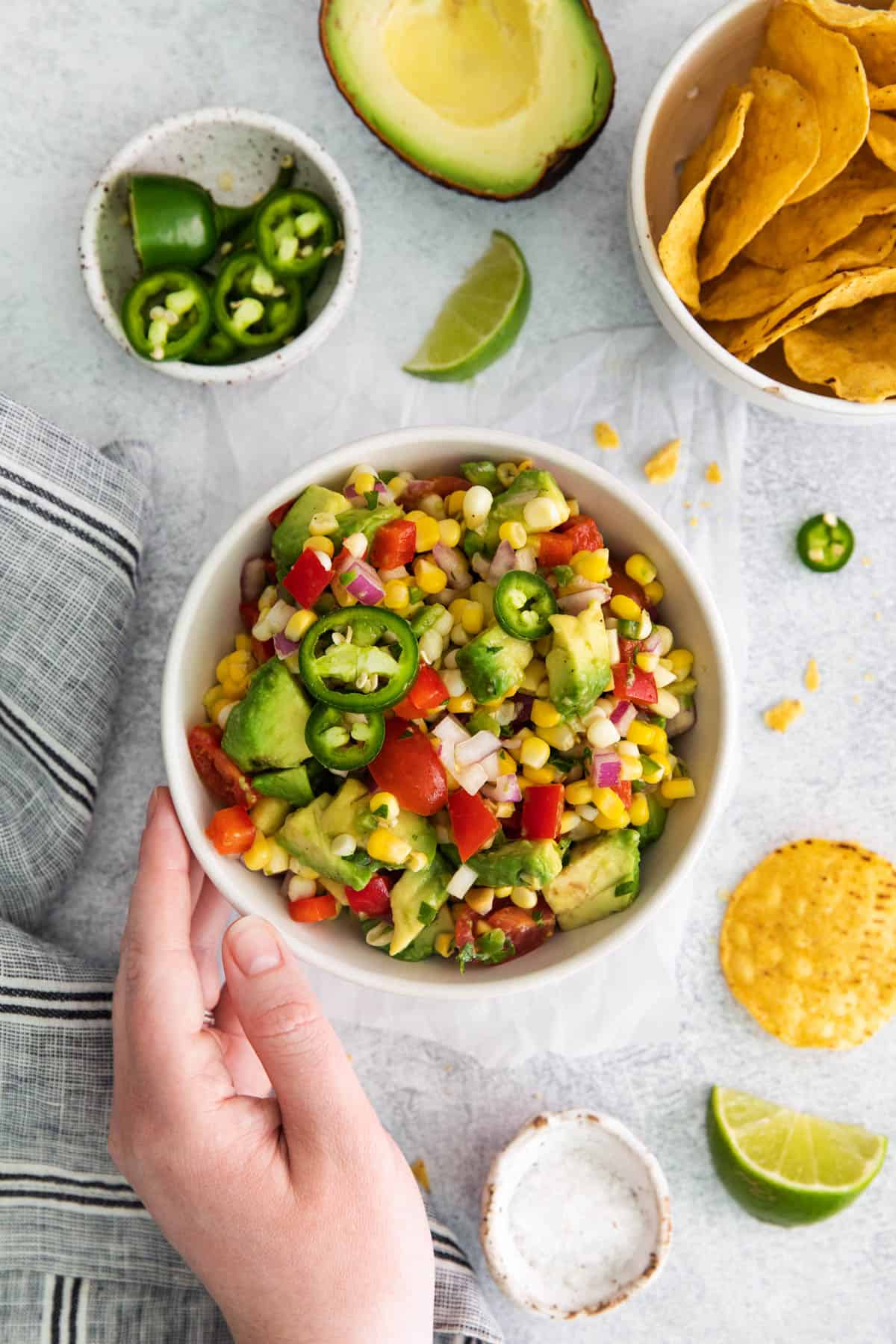 A hand reaching for a bowl of corn and avocado salad.