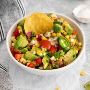 A bowl of corn and avocado salad with a tortilla chip in it.