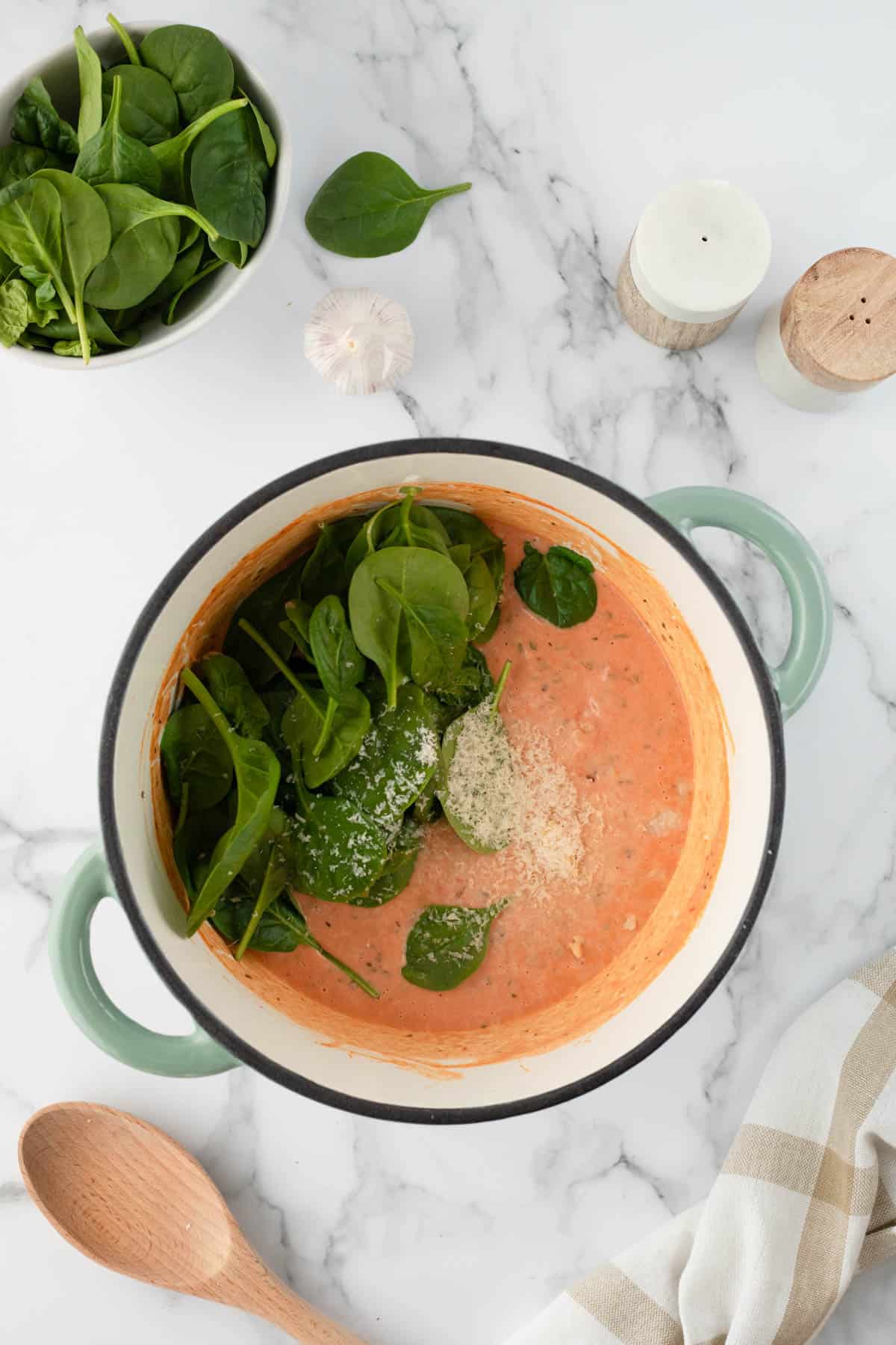 Adding fresh spinach to pink sauce in a large pot.